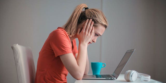 Mujer con una camisa naranja sentada en la mesa, mirando su computadora portátil.