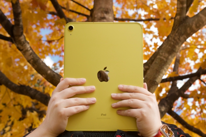 Alguien sosteniendo el iPad amarillo (2022) frente a árboles con hojas naranjas y amarillas.