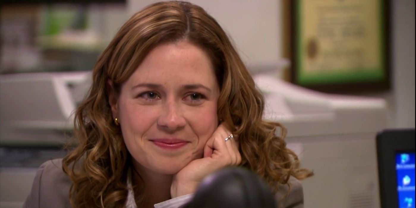 Pam sonríe mientras apoya su rostro en su mano en The Office.