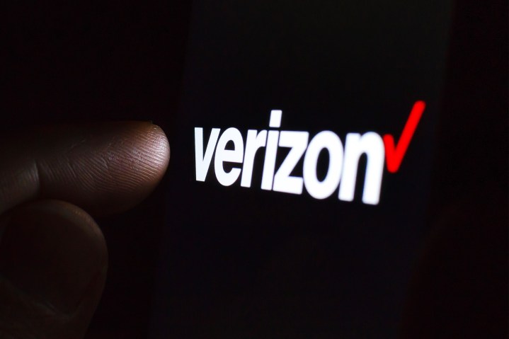 Logotipo de Verizon en la pantalla de un teléfono inteligente en una habitación oscura y un dedo tocándolo.