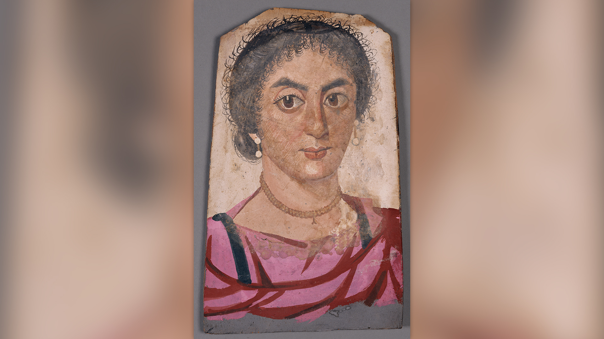 En este retrato, una mujer lleva aretes de perlas, un collar, una túnica rosa intenso y clavi negros, o tiras verticales de ornamentación.  Su cabello rizado está recogido en un moño.