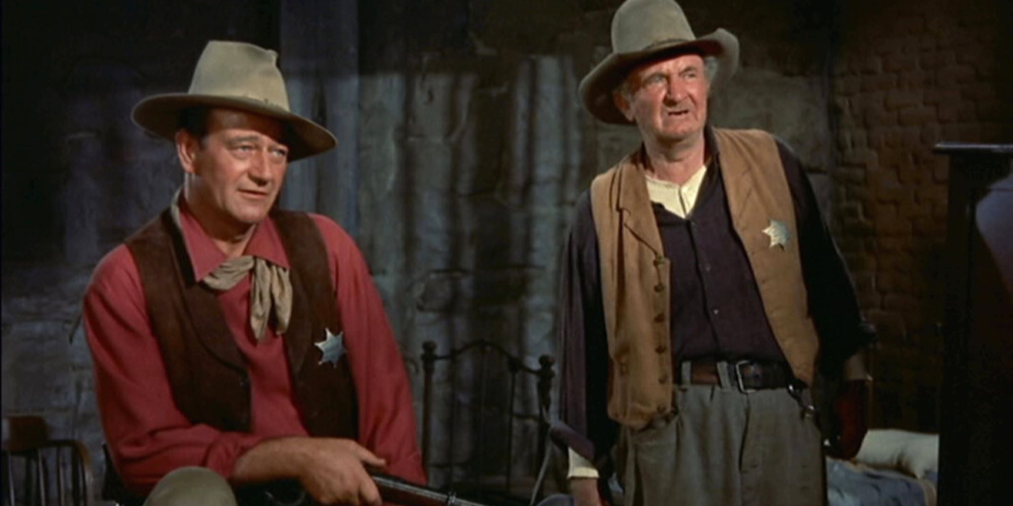 John Wayne sentado y Walter Brennan de pie junto a él en Río Bravo