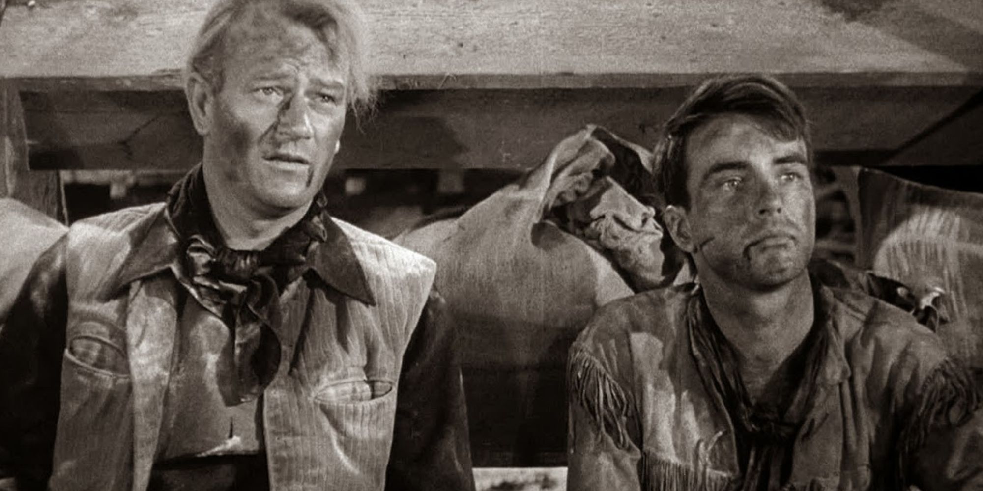 John Wayne y Montgomery Clift sentados uno al lado del otro en el suelo mirando hacia adelante en Red River