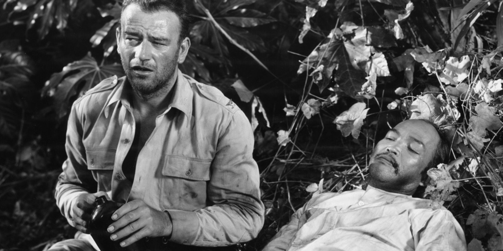 John Wayne mirando hacia un lado mientras está sentado junto a un hombre tumbado en el césped en Sands of Iwo Jima-1