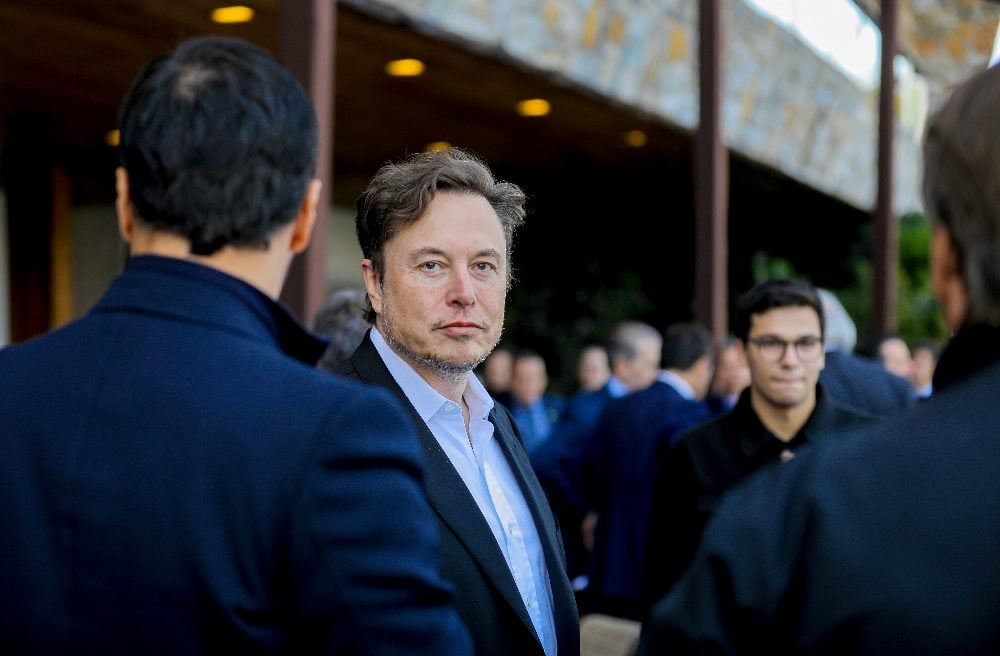 Elon Musk, vestido con un traje azul y una camisa azul, camina por la calle entre una multitud hablando sobre la resonancia de la marca.