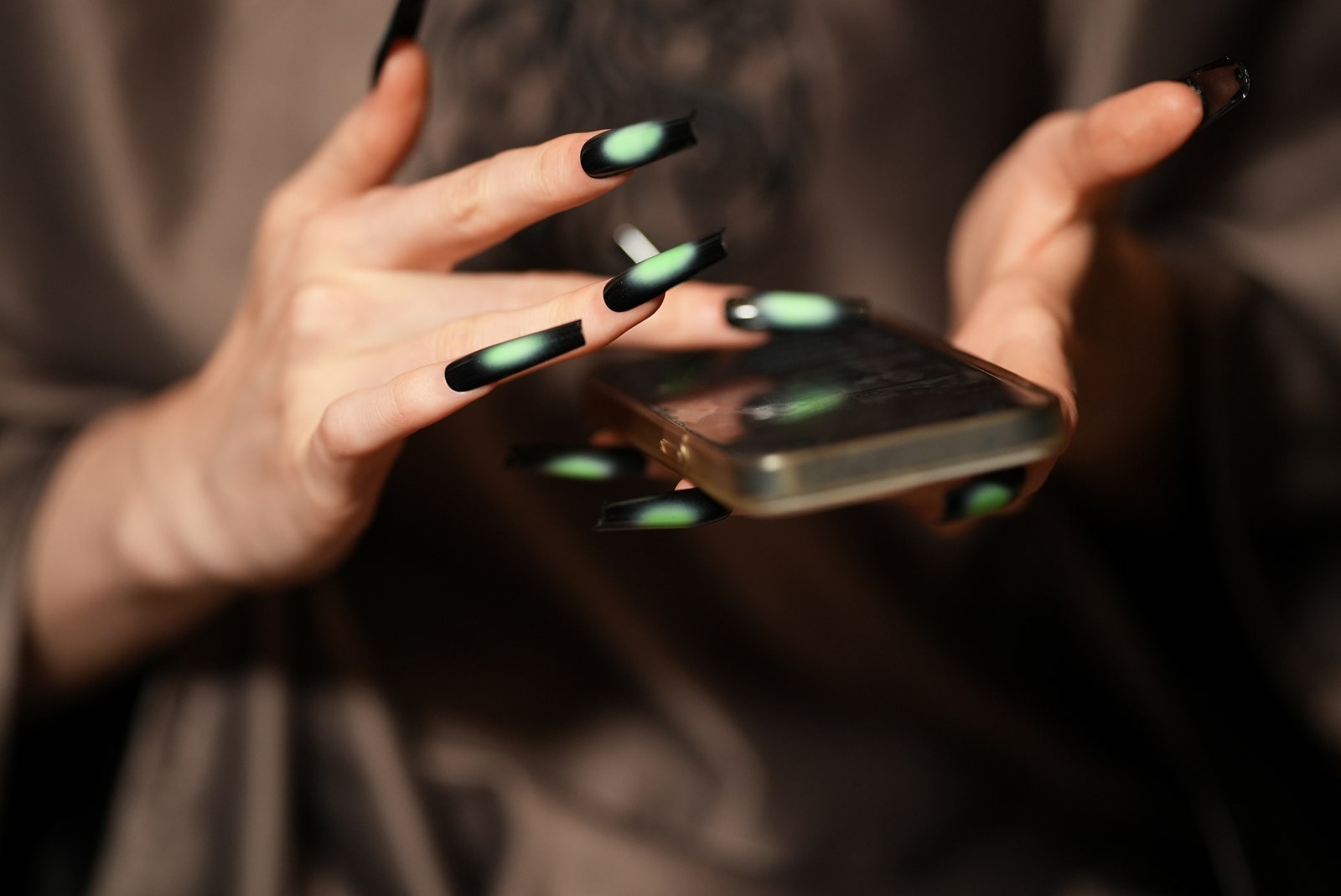 Manos escribiendo en un teléfono con uñas pintadas con un diseño negro y verde.
