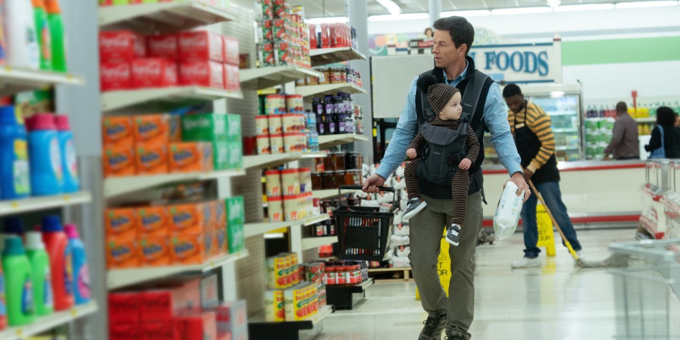 Dan Morgan (Mark Wahlberg) usando un portabebés mientras camina por una tienda de comestibles en The Family Plan.