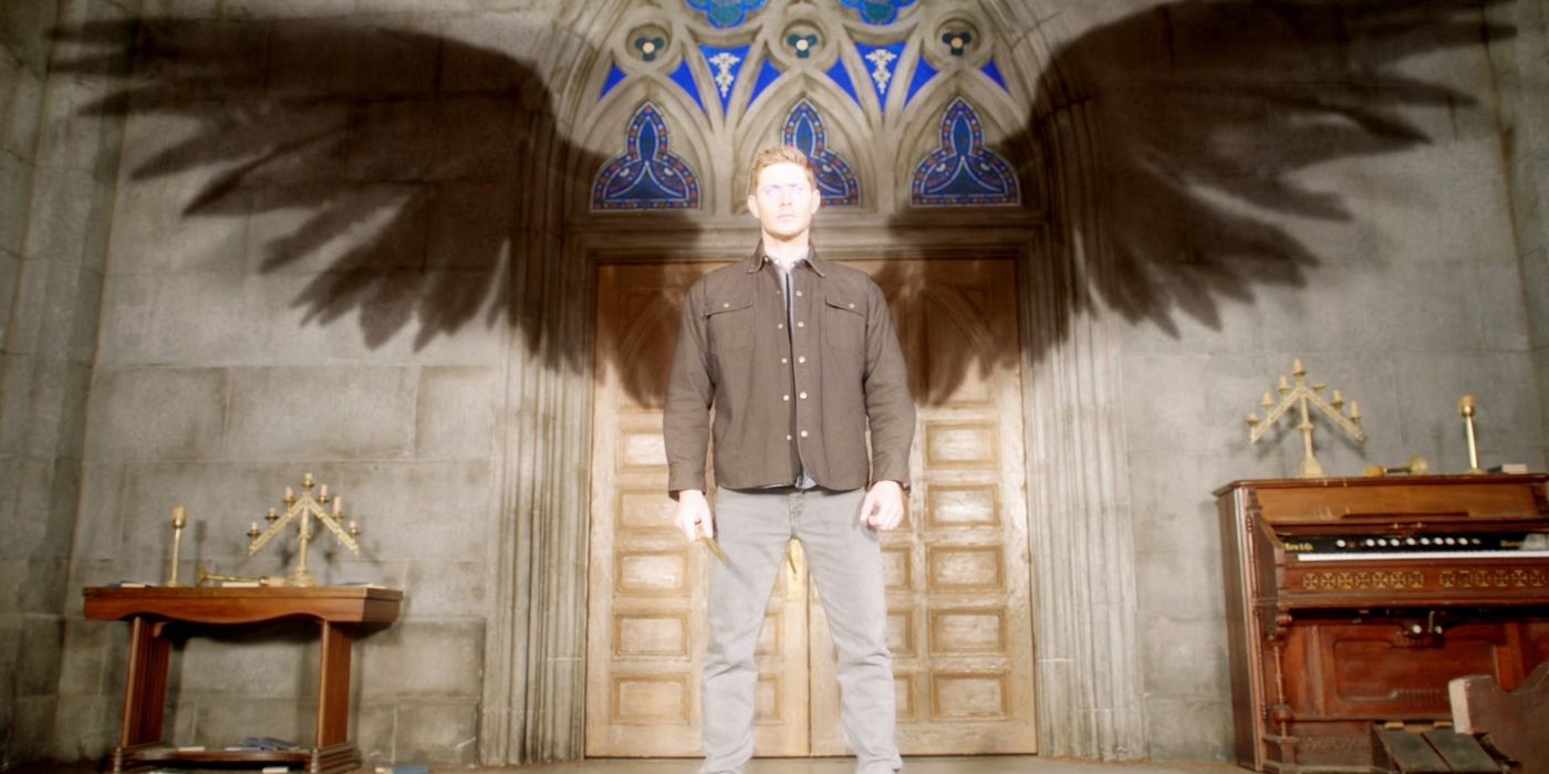 The archangel Michael, using Dean Winchester as a vessel, stands in a church as light is cast upon him with his angel wings casting a shadow on the wall behind him.