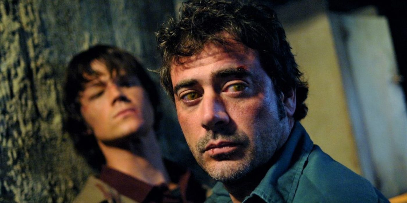 John Winchester, possessed by Azazel, holds Sam against a wall as he turns to look behind him.