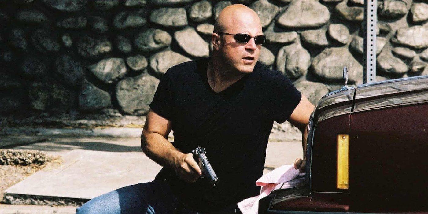 Michael Chiklis with a gun crouched behind a car in The Shield