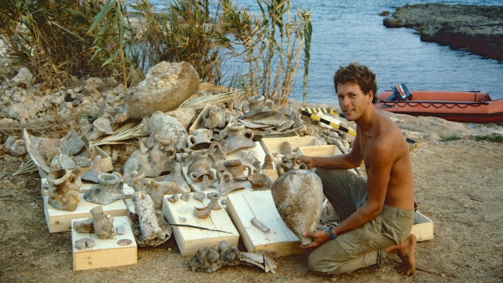 Un hombre sentado en una playa con decenas de artefactos.