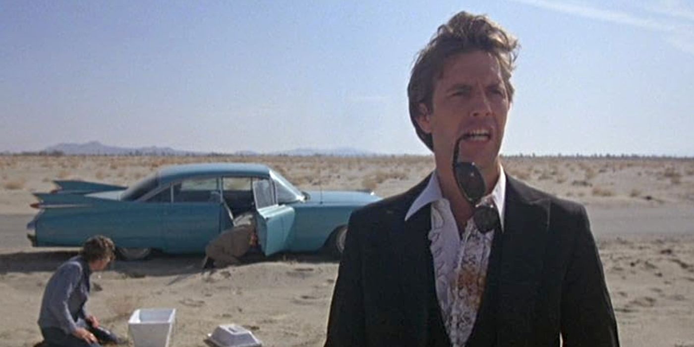 Kevin Costner as Gardner Barnes, standing by a car in the desert holding his sunglasses between his teeth in Fandango