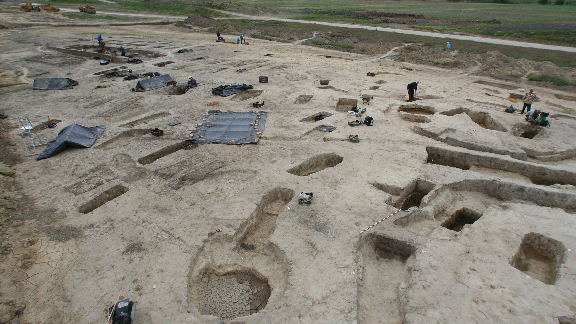 Fotografía de paisaje del sitio de excavación, que muestra agujeros de diferentes formas excavados en el campo de tierra apisonada.