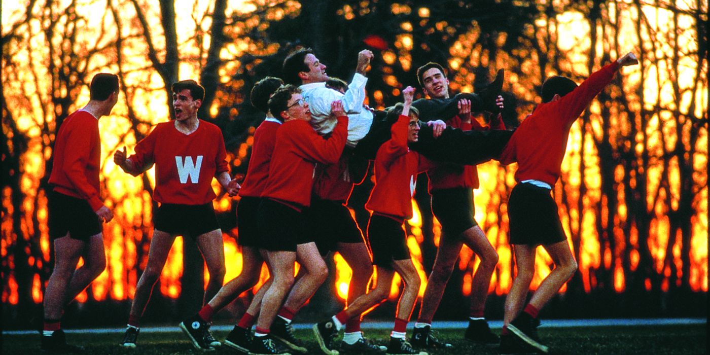 Un grupo de estudiantes vestidos con uniformes deportivos rojos y negros y llevando alegremente a John Keating (Robin Williams) a través de un campo en Dead Poets Society.