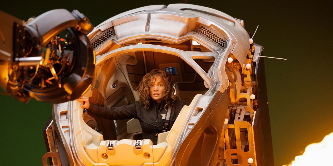 Jennifer López montando un traje robótico frente a una pantalla verde en una toma detrás de escena de Atlas.